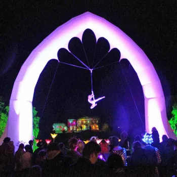 An acrobat hanging from a 12 foot inflatable arch at night
