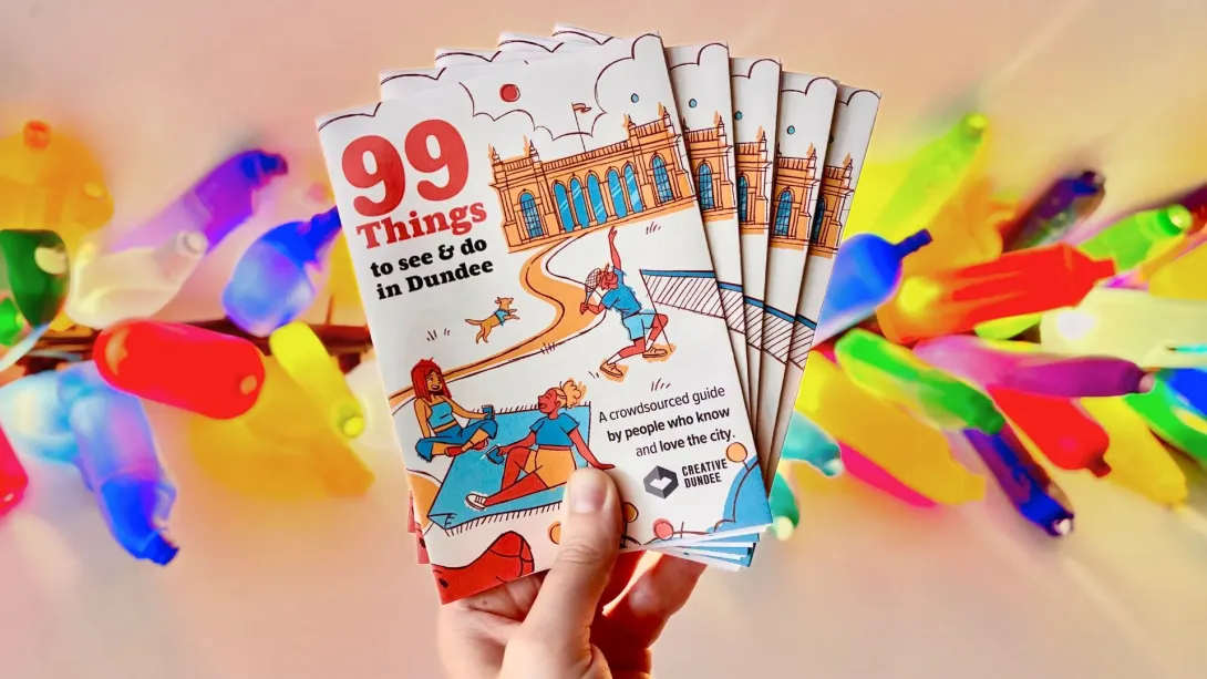 Hand holding a small pile of the 99 Things guide